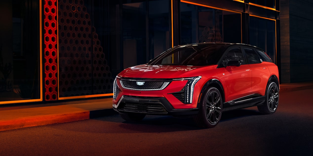 Cadillac OPTIQ 2027 en color Radiant Red frente a una fachada iluminada